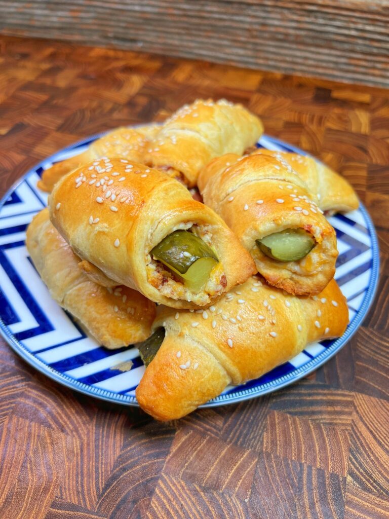 a blue and white plate with dill pickles in a blanket of crescent dough with cream cheese filling and sesame seeds on top.