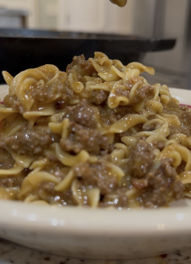 A close-up of a plate of pasta mixed with ground beef and sauce, served on a white dish with a blurred kitchen background.