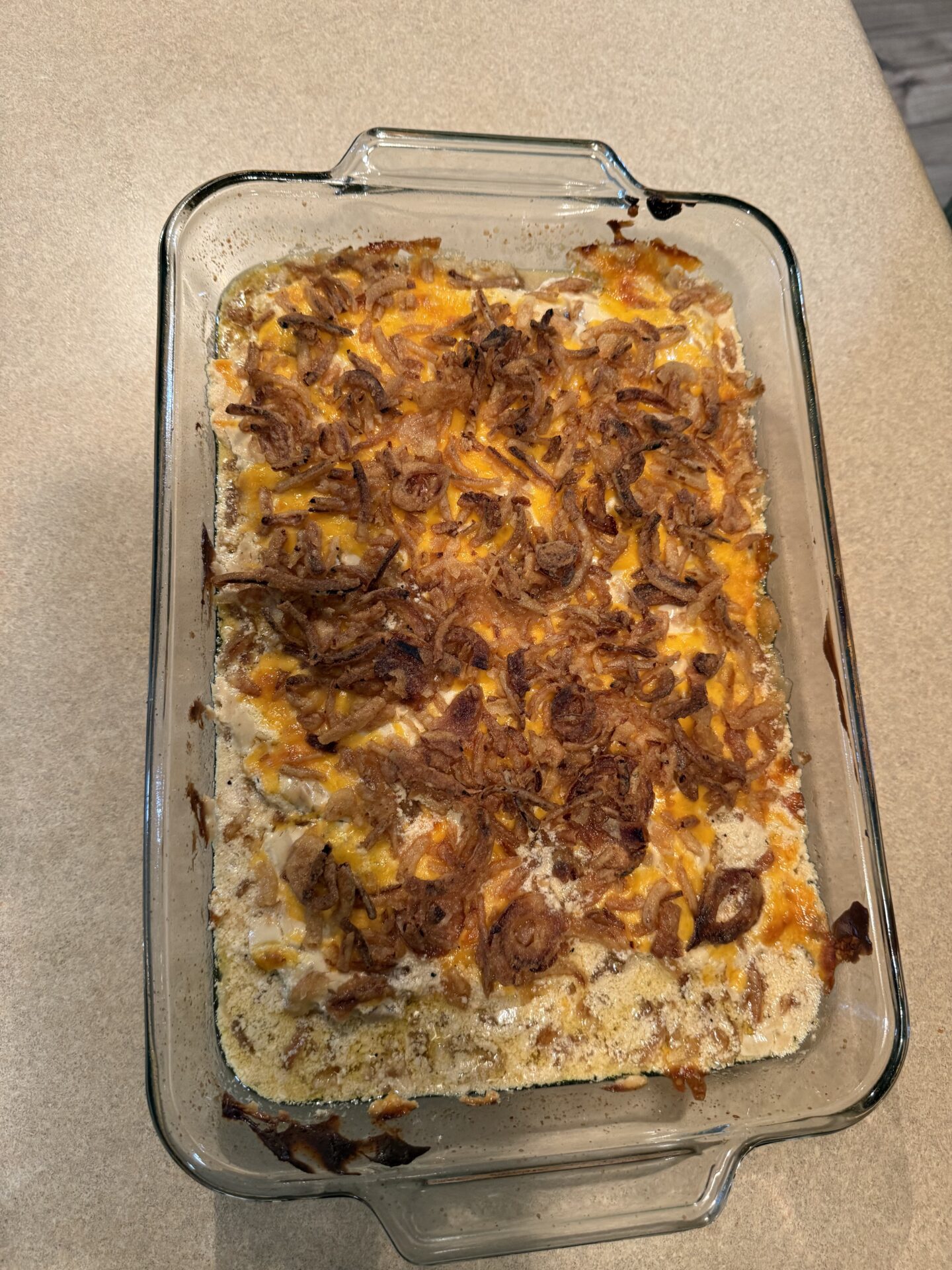 A glass baking dish filled with a casserole topped with browned, crispy fried onions and melted cheese, sitting on a beige countertop.