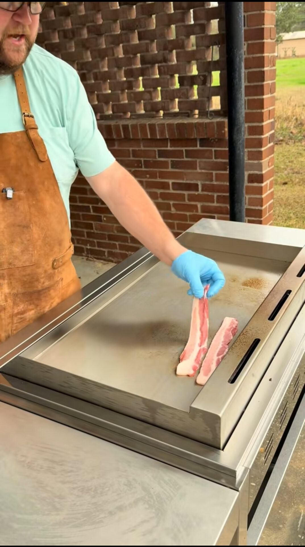 A person holding meat on a grill.