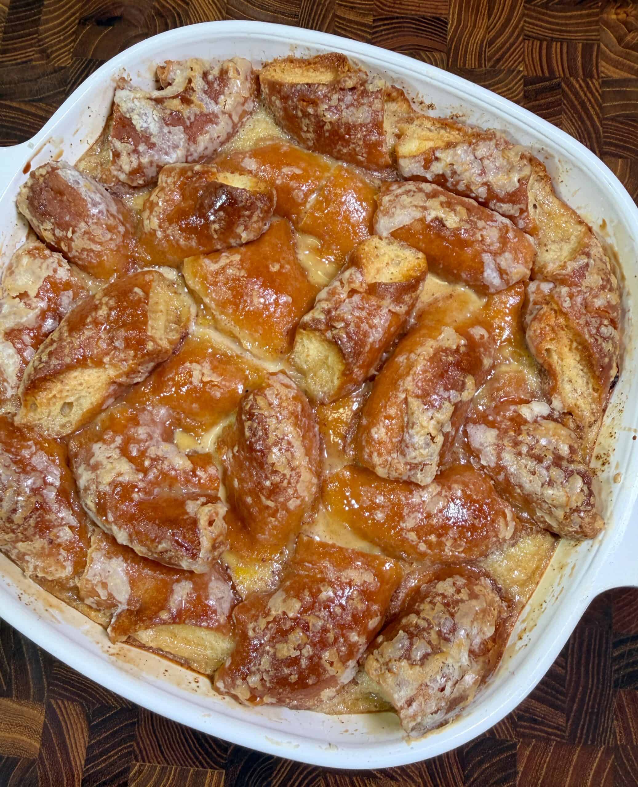 A white baking dish filled with golden-brown pretzel bread pudding, with visible chunks of soft pretzel pieces coated in a glossy, baked custard and a light sugary glaze on top.