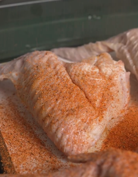 Raw chicken wings covered with a generous layer of orange and brown seasoning, placed in a glass dish, ready to be cooked.