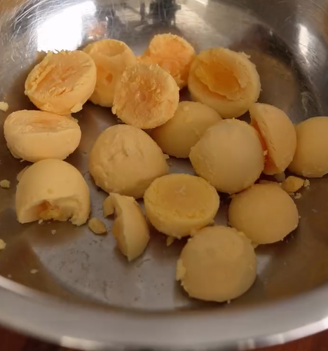A metal bowl containing several cooked and halved hard-boiled egg yolks, some intact and some slightly crumbled.