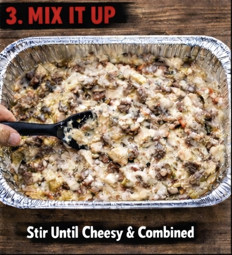 A hand holds a black spoon, mixing a cheesy bean mixture in a foil tray. Text at the top reads 3. MIX IT UP and at the bottom reads Stir Until Cheesy & Combined. The tray sits on a wooden surface.