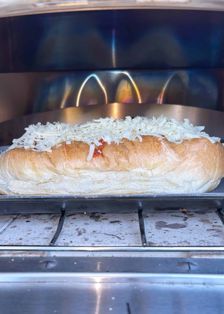 A sandwich roll topped with shredded cheese is being toasted in an oven, with the cheese beginning to melt.