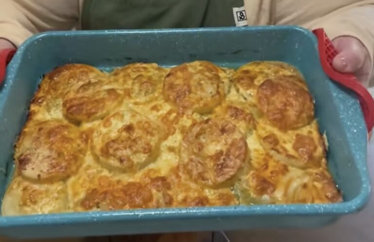 A person holds a blue baking dish filled with golden-brown, cheesy scalloped potatoes fresh from the oven, with browned melted cheese on top.