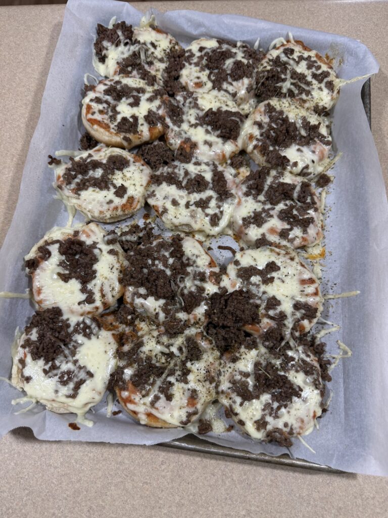 A baking sheet lined with parchment paper holds several mini pizzas topped with melted cheese and crumbled cooked ground beef. The pizzas appear freshly baked and arranged closely together.