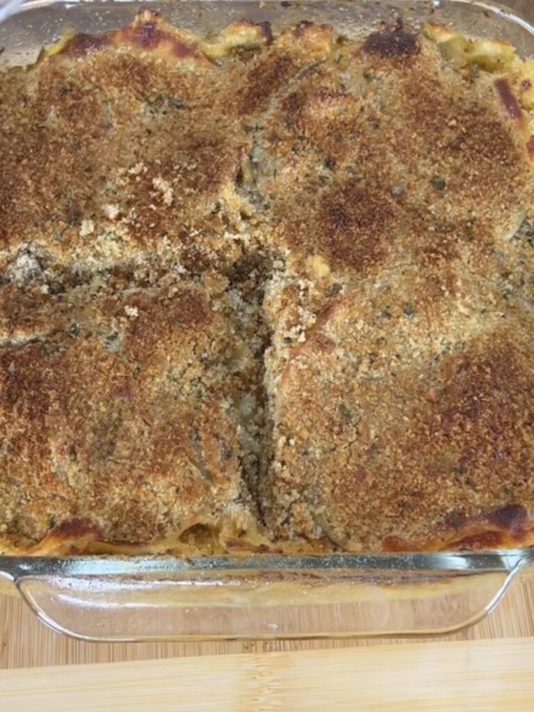 A glass baking dish filled with a golden-brown casserole topped with a crispy breadcrumb crust, with one serving removed from the center.