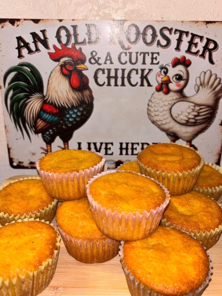 A group of golden muffins stacked in front of a colorful sign featuring a rooster and a hen that reads, An old rooster & a cute chick live here.