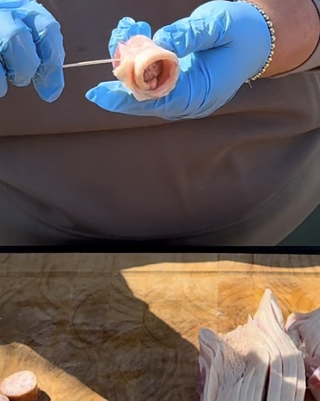 A person wearing blue gloves wraps bacon around a large sausage slice using a wooden skewer, with more bacon and sausages on a wooden cutting board in the foreground.