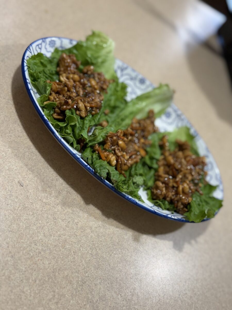 A patterned plate holds three lettuce leaves topped with a savory mixture of ground meat and vegetables, arranged on a light brown countertop.