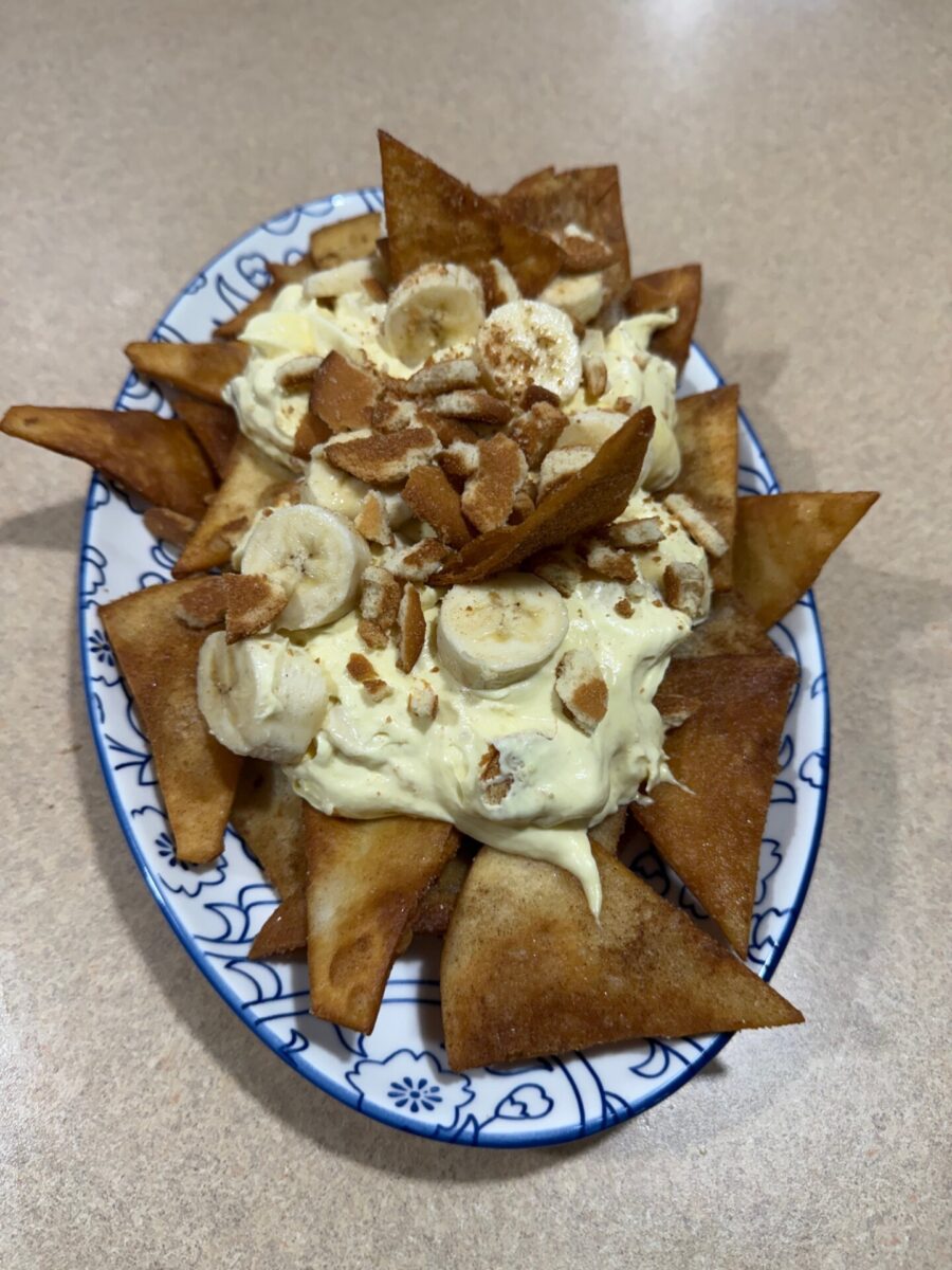 A plate of fried tortilla chips topped with banana slices, creamy pudding, and crushed nuts, served on a decorative oval dish atop a beige countertop.