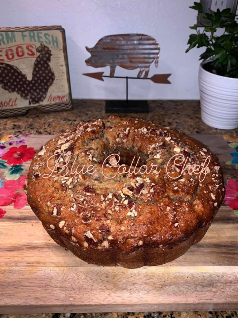 A golden brown bundt cake topped with chopped nuts sits on a wooden board. In the background are a pig-shaped decoration and a vintage “Farm Fresh Eggs” sign. The text “Blue Collar Chef” overlays the image.