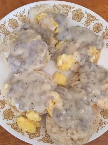 A plate with six biscuit halves topped with scrambled eggs and creamy sausage gravy, served on a white plate with a gold floral pattern.