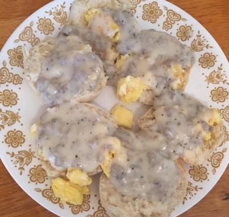 A plate with six biscuit halves topped with scrambled eggs and covered in creamy sausage gravy, served on a white plate with a gold floral pattern.
