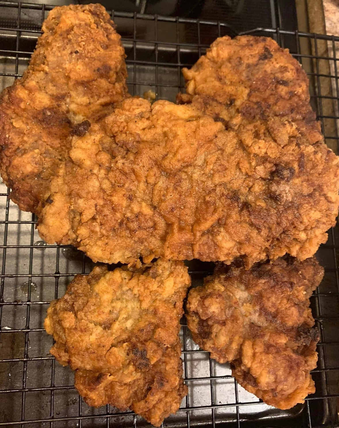 Several pieces of golden-brown fried chicken are cooling on a black wire rack. The chicken has a crispy, textured coating and appears freshly cooked.