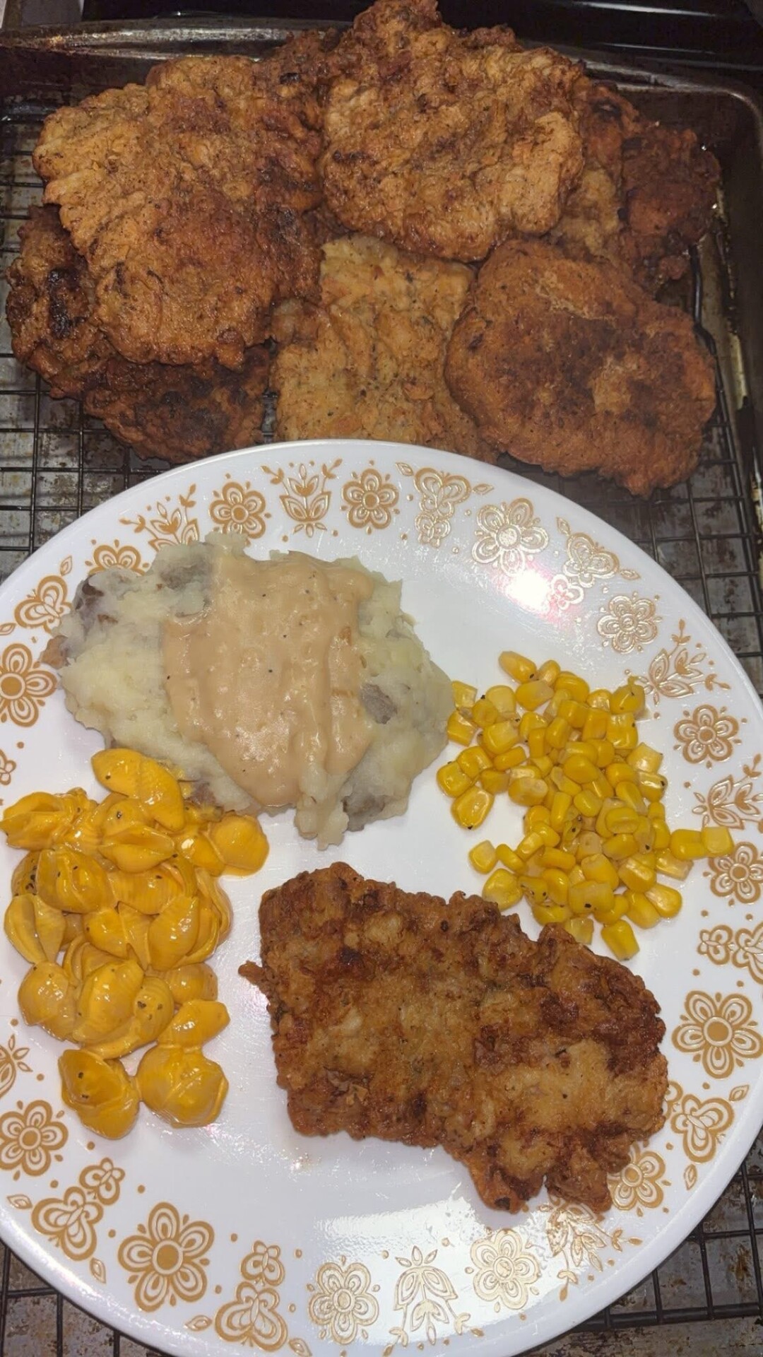 A plate with fried chicken, mashed potatoes and gravy, macaroni and cheese, and corn sits in front of a tray of additional pieces of fried chicken.