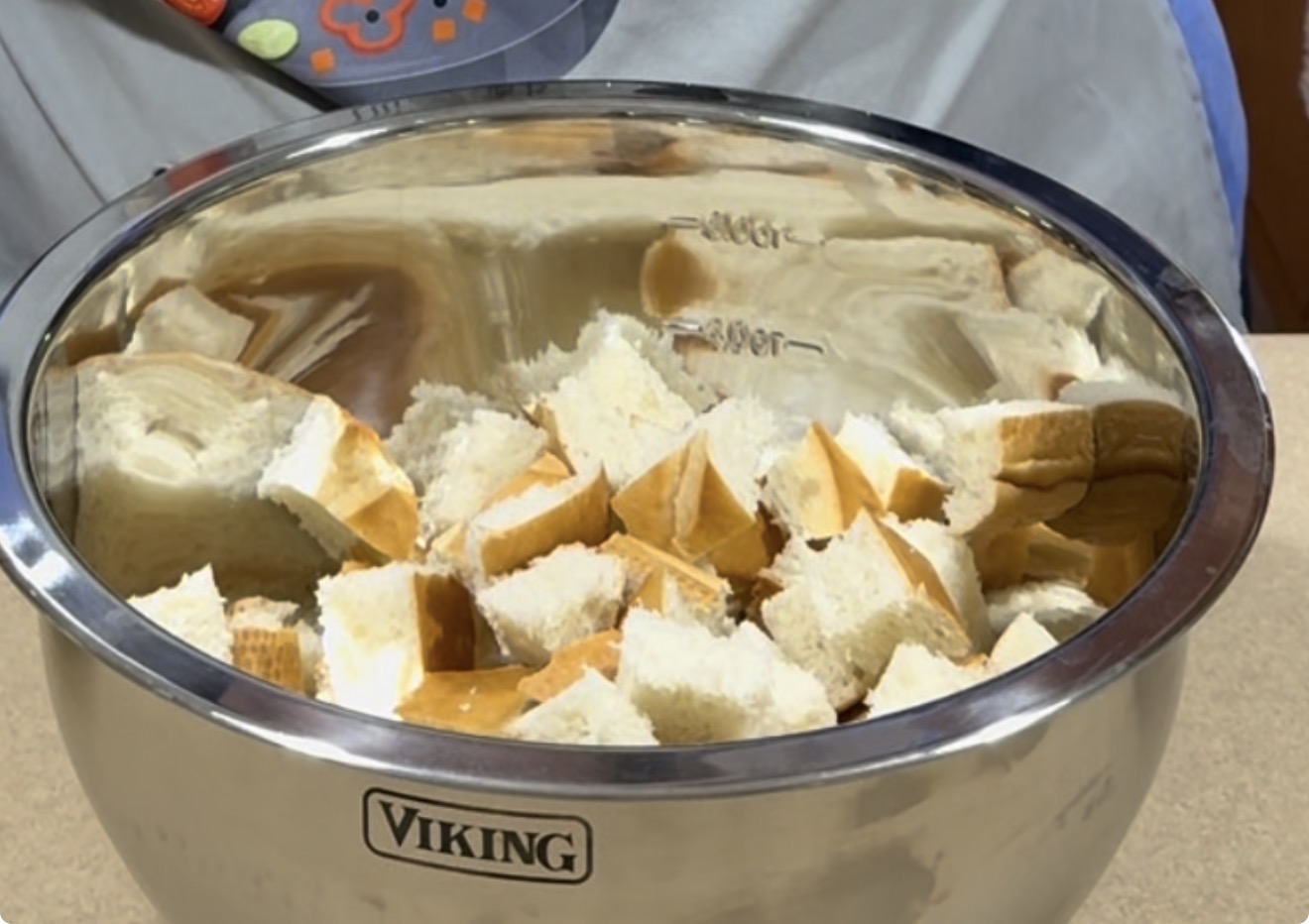 A stainless steel mixing bowl labeled Viking filled with cubed pieces of bread sitting on a countertop.