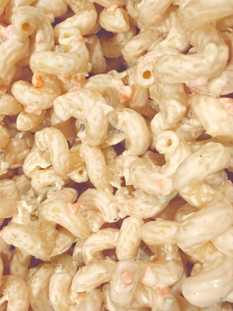 Close-up of creamy macaroni salad with elbow pasta, small bits of vegetables like carrots and green peppers, all coated in a thick, pale dressing.