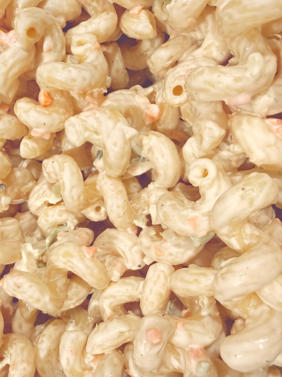 Close-up of creamy macaroni salad with elbow pasta, small bits of vegetables like carrots and green peppers, all coated in a thick, pale dressing.