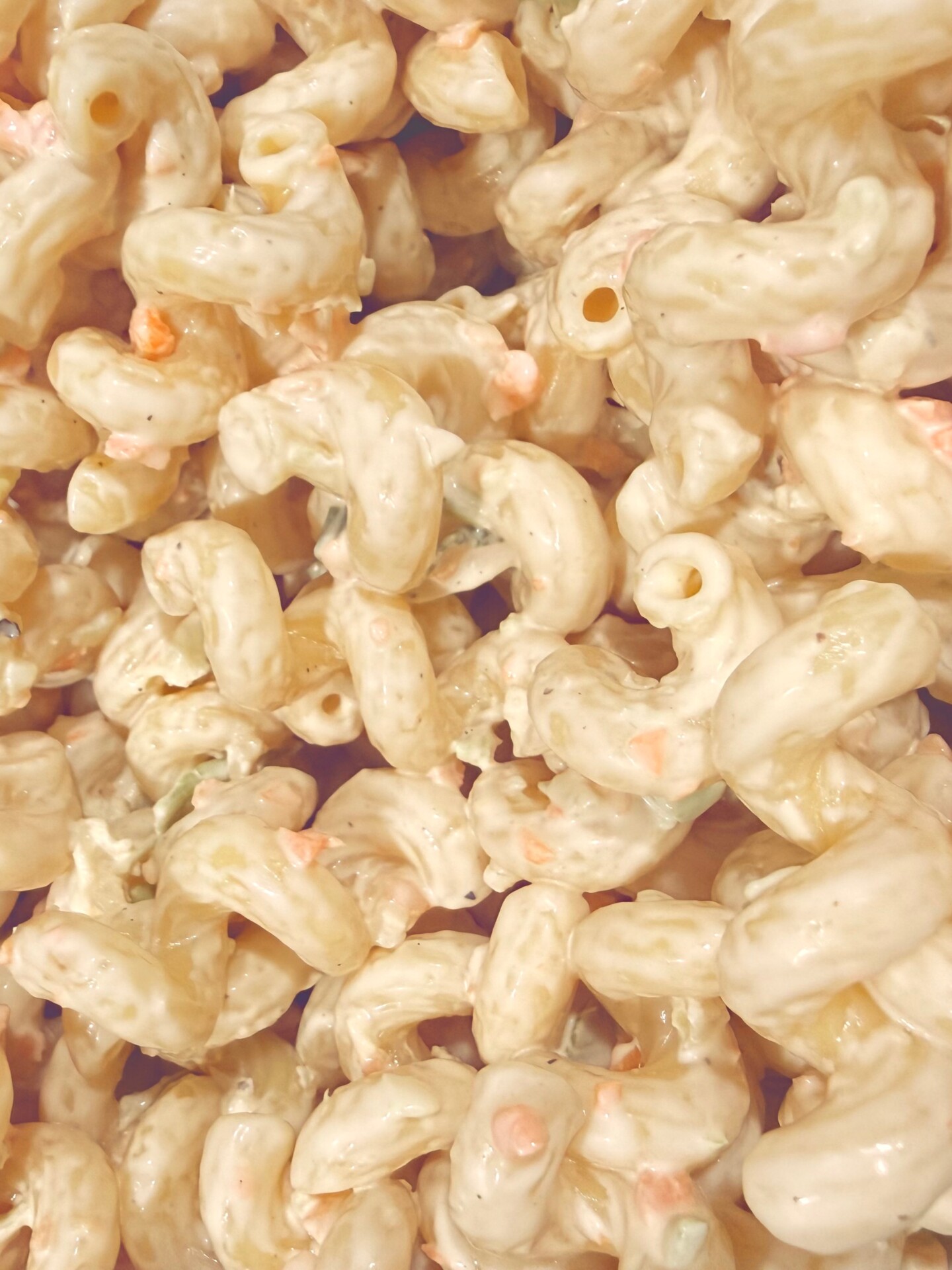 Close-up of creamy macaroni salad with elbow pasta, small bits of vegetables like carrots and green peppers, all coated in a thick, pale dressing.