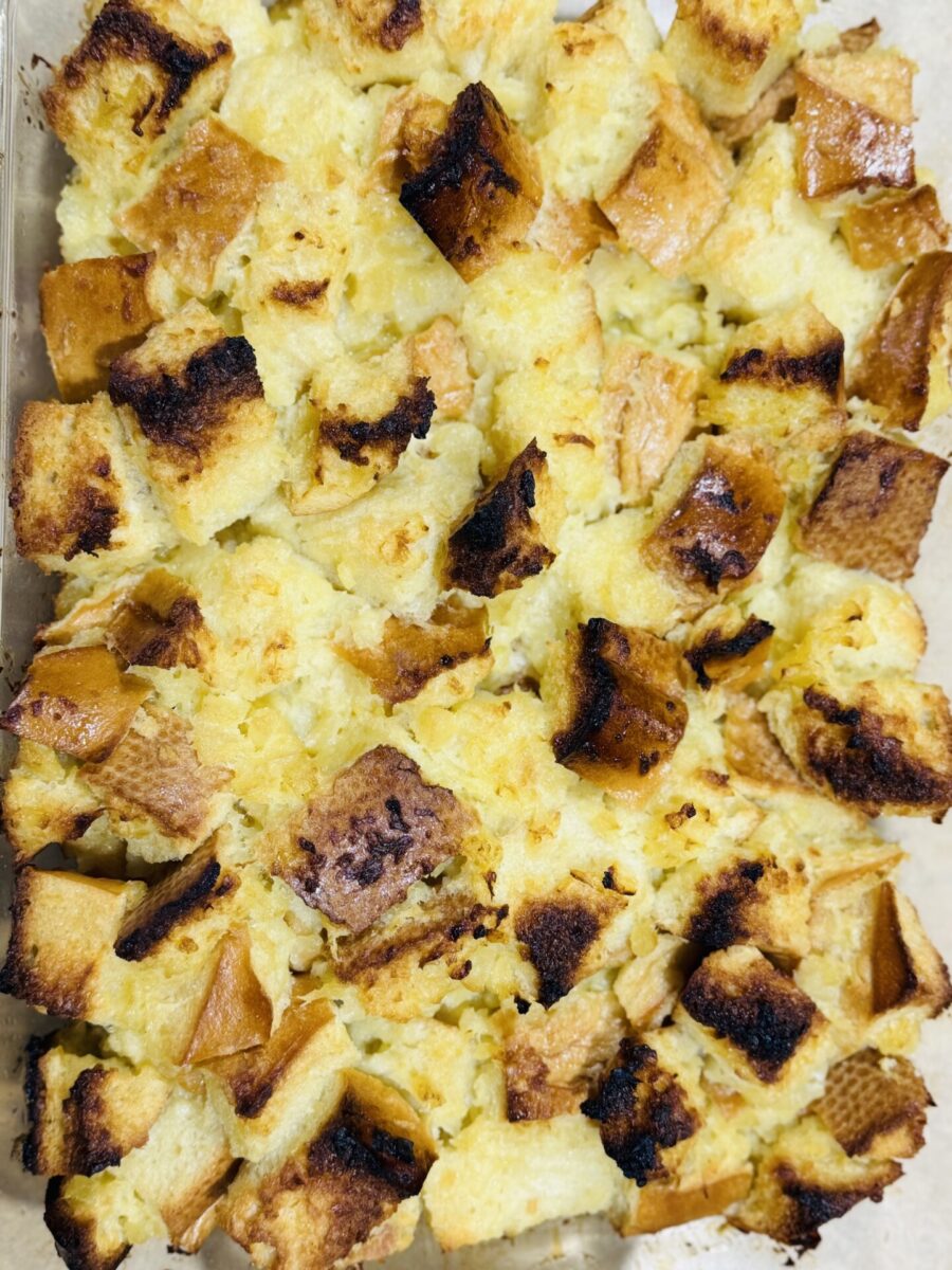 A close-up of golden-brown bread pudding, showing toasted cubes of bread with a creamy, custard-like texture in between, baked until crisp on top.