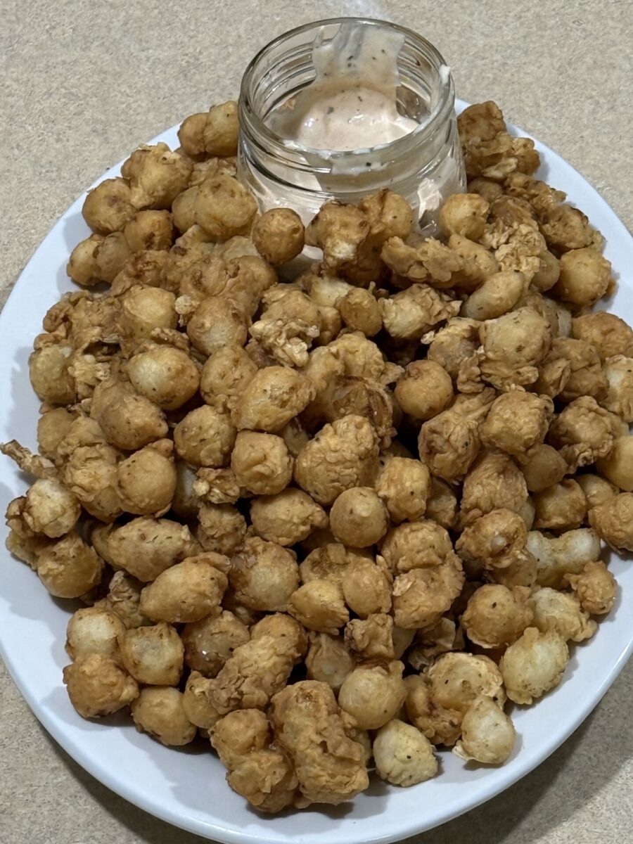 A white plate filled with a pile of small, golden-brown fried bites, served with a partially empty glass jar of creamy dipping sauce in the center. The plate rests on a beige countertop.