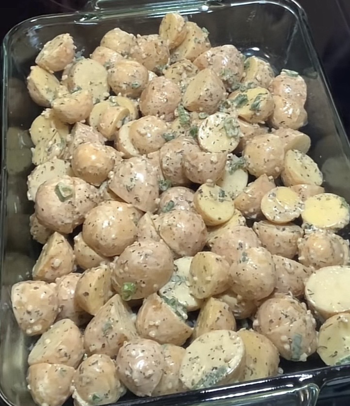 A glass baking dish filled with halved baby potatoes coated in a creamy herb seasoning, ready to be baked.