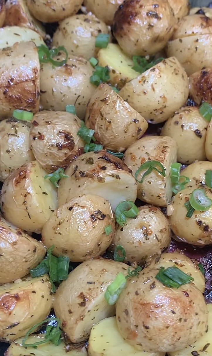 Roasted baby potatoes with herbs and spices, garnished with chopped green onions. The potatoes are golden brown and appear crispy on the outside.