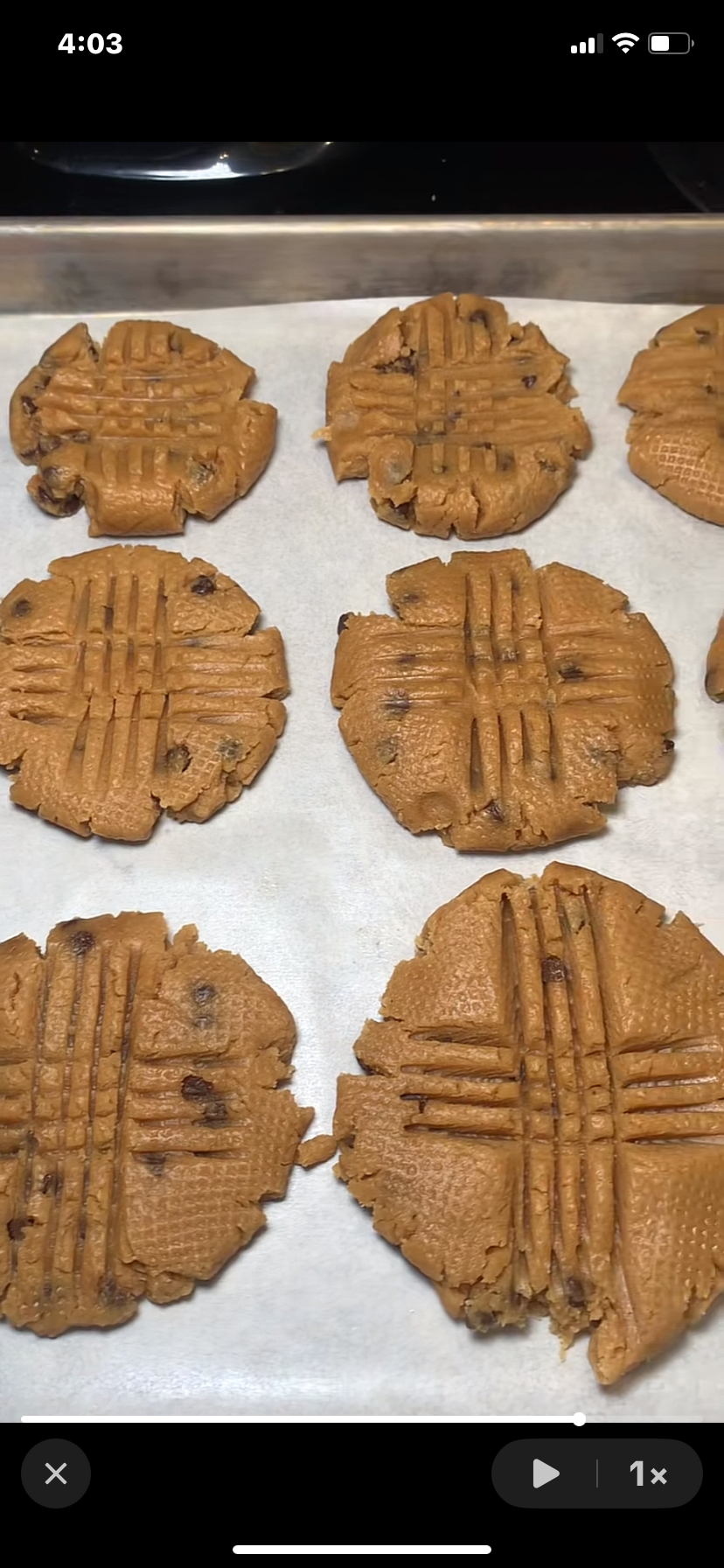 Eight unbaked peanut butter cookies with crosshatch fork marks are arranged on a parchment-lined baking sheet, ready to go into the oven. The cookies have a slightly rough texture and visible chocolate chips.