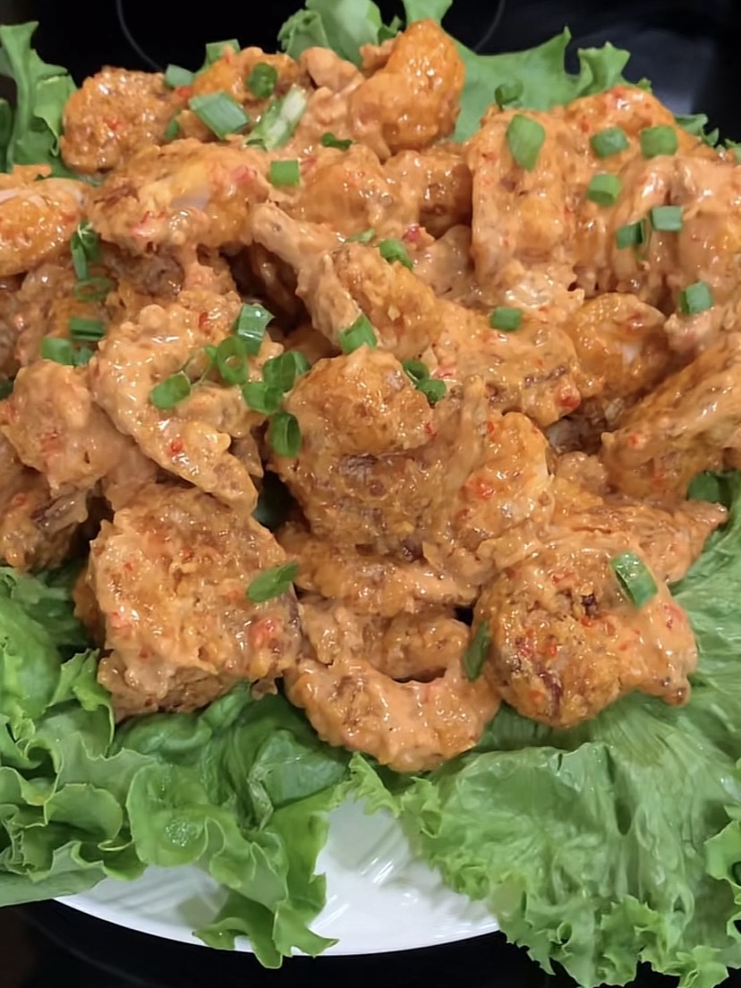 A plate of crispy, saucy chicken pieces garnished with chopped green onions is served on a bed of fresh green lettuce leaves.