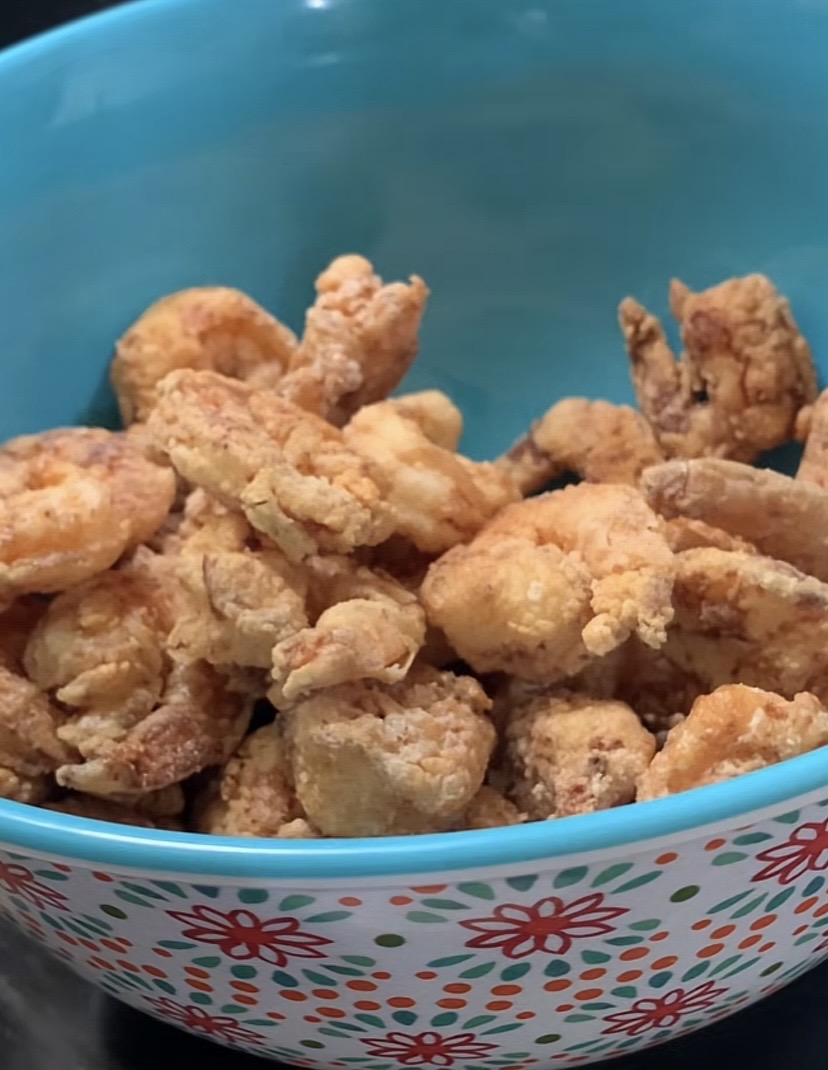 A blue bowl with a colorful floral pattern holds a serving of golden-brown fried shrimp.