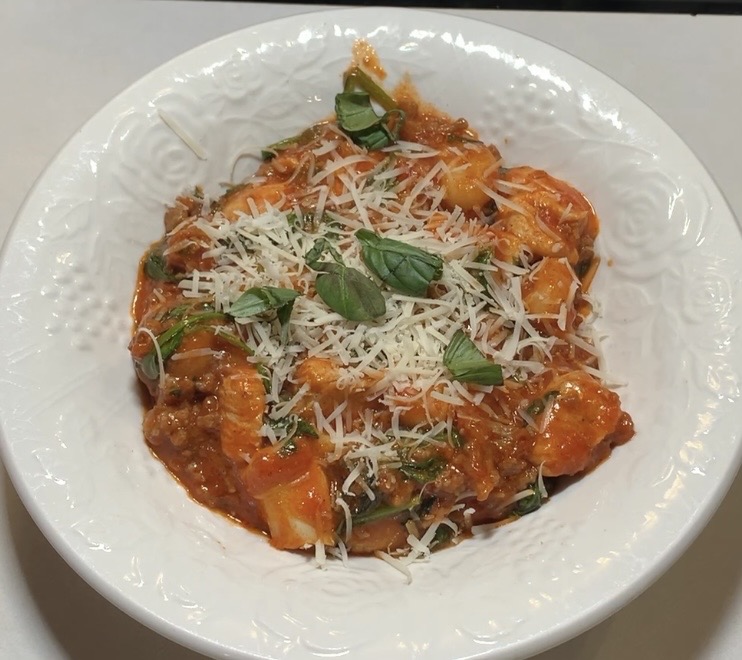 A white bowl filled with pasta in red tomato sauce, topped with grated parmesan cheese and fresh basil leaves.