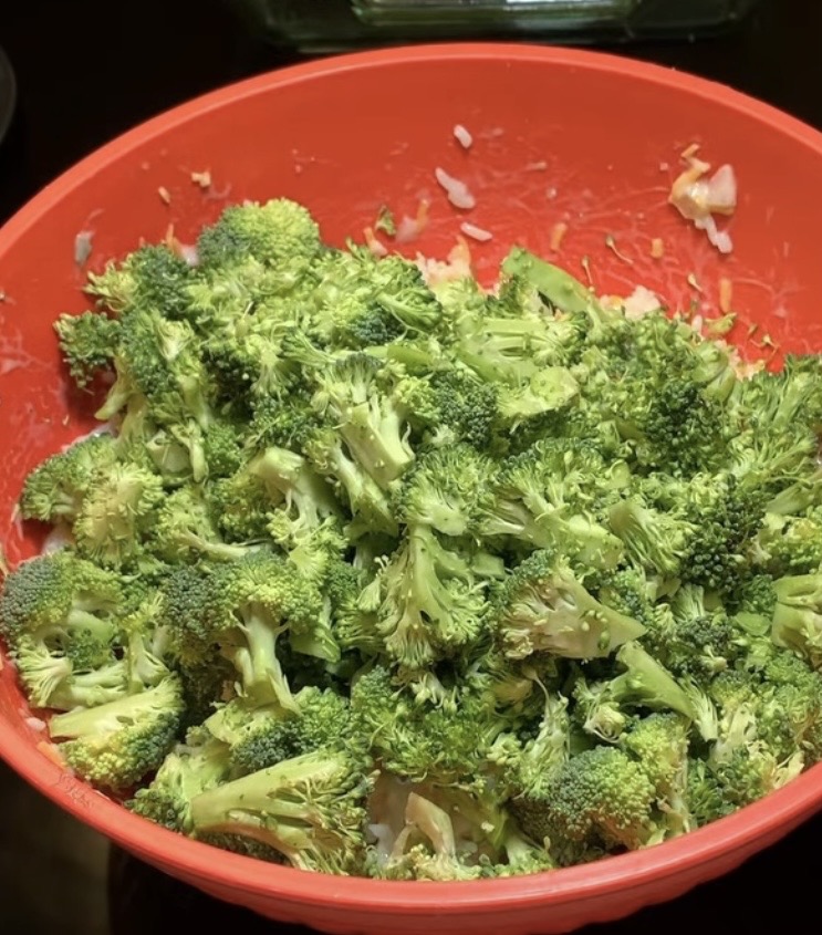 A large red bowl filled with fresh chopped broccoli florets and some diced onions, ready for cooking or salad preparation.