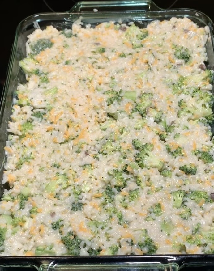 A glass baking dish filled with a mixture of chopped broccoli, rice, shredded cheese, and a creamy sauce, ready to be baked as a casserole.