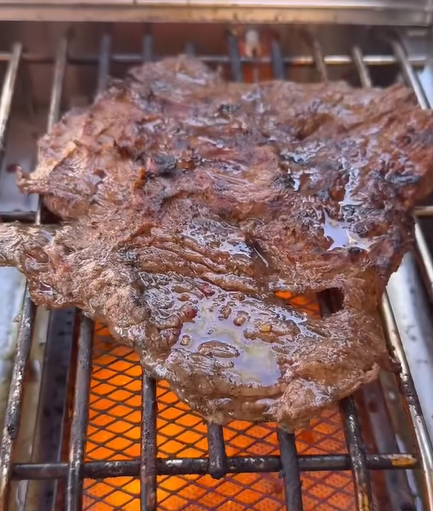 A juicy, grilled steak sizzling on a barbecue grill over an open flame, with grill marks and glistening juices on the meat.