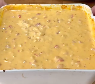 A close-up of a baking dish filled with creamy, orange-yellow cheese dip with chunks of tomato and spices visible throughout.