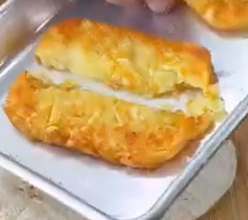 A golden-brown hash brown is split in half on a metal tray, revealing its crispy outside and soft interior.