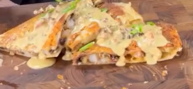 A close-up of sliced quesadillas topped with creamy sauce and garnished with green herbs, displayed on a wooden serving board.