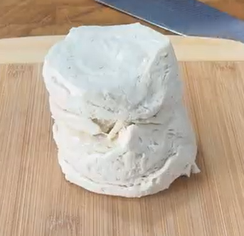 A stack of uncooked biscuit dough rounds on a wooden cutting board, with a metal knife partially visible in the background.