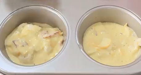 Two muffin tin cups filled with a creamy yellow mixture containing chunks of potatoes and seasoning, ready to be baked.