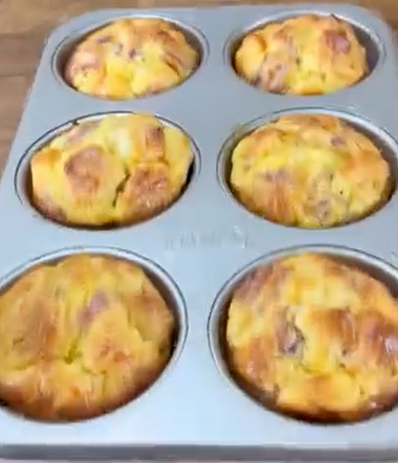 A muffin tray filled with six golden-brown, freshly baked muffins, sitting on a wooden surface.