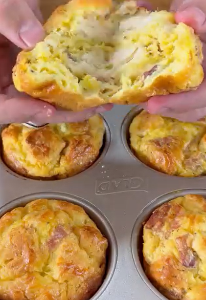 A person splits open a freshly baked savory muffin, revealing a soft, fluffy interior. The muffin tray below holds five more golden-brown muffins.