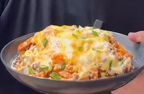 A person holds a bowl filled with cheesy, baked fries topped with ground meat, melted cheese, and chopped green onions.