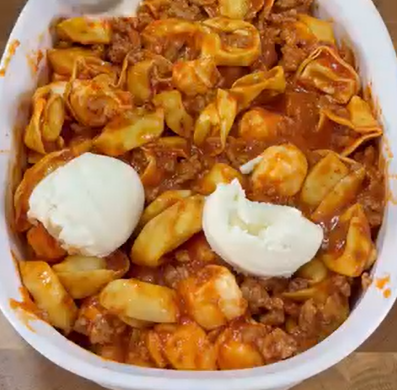 A white dish filled with cheese tortellini in tomato meat sauce, topped with two scoops of ricotta cheese, one of which is slightly broken apart.