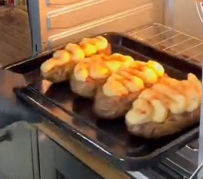 A person is placing a baking tray with four twice-baked potatoes, topped with piped mashed potato, into an oven.