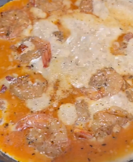 Shrimp cooking in a creamy, orange-colored sauce with visible herbs and spices, simmering in a pan.