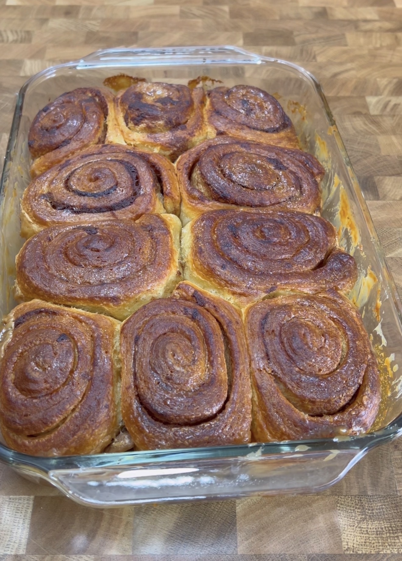 A glass baking dish filled with nine golden-brown cinnamon rolls, arranged in three rows, sitting on a wooden countertop.