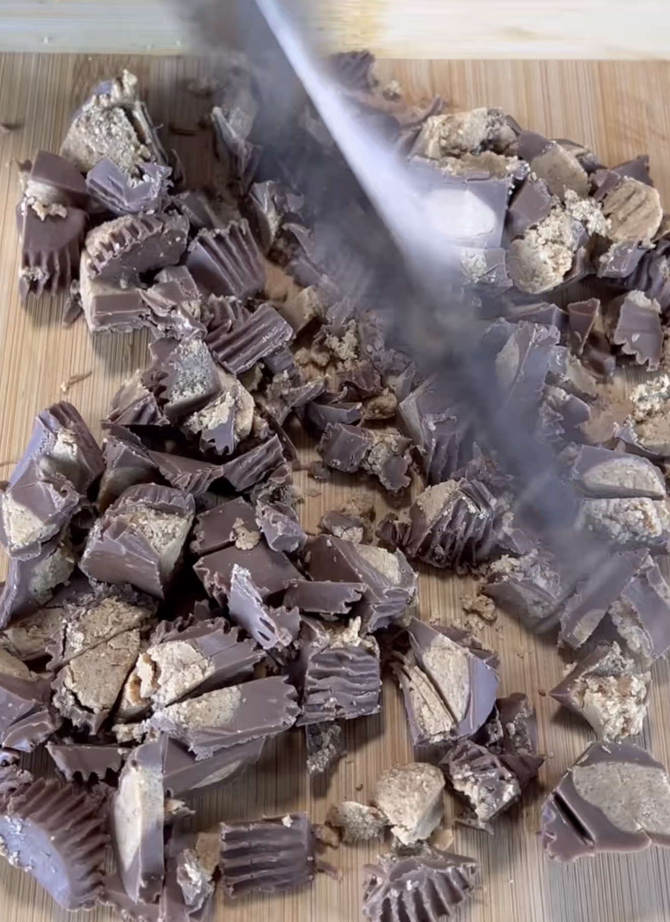 Chopped peanut butter cups being cut with a large knife on a wooden cutting board.