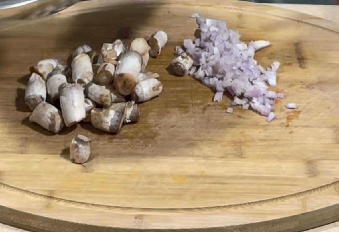 A wooden cutting board with chopped mushrooms on the left and finely diced onions on the right.